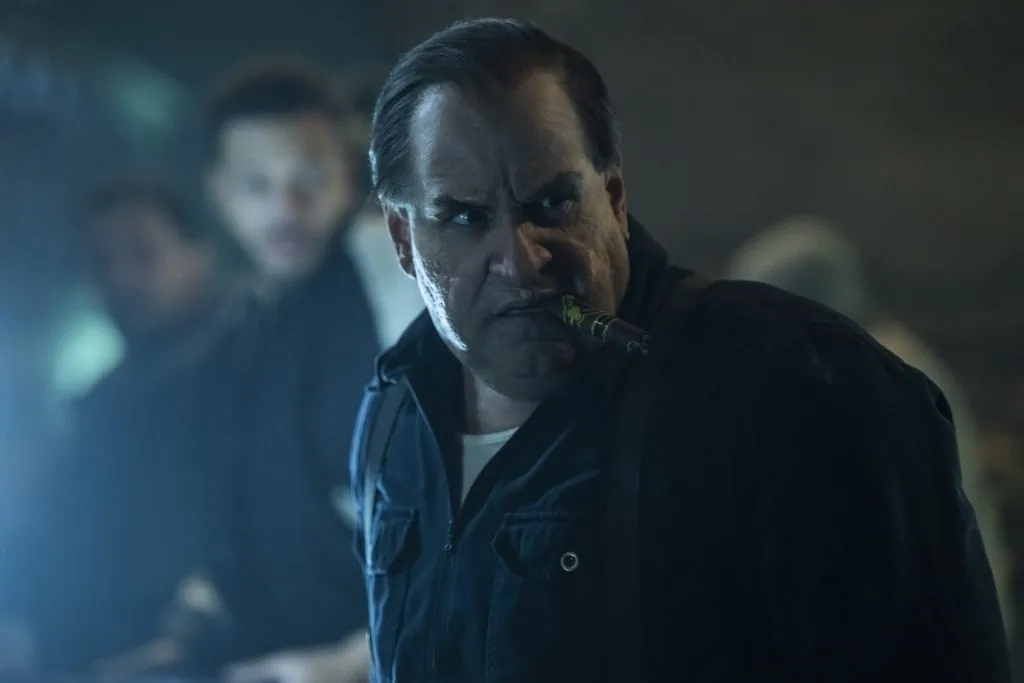 Un uomo dall'aspetto serio, con una giacca nera e una sigaretta in bocca, in un ambiente buio e drammatico.