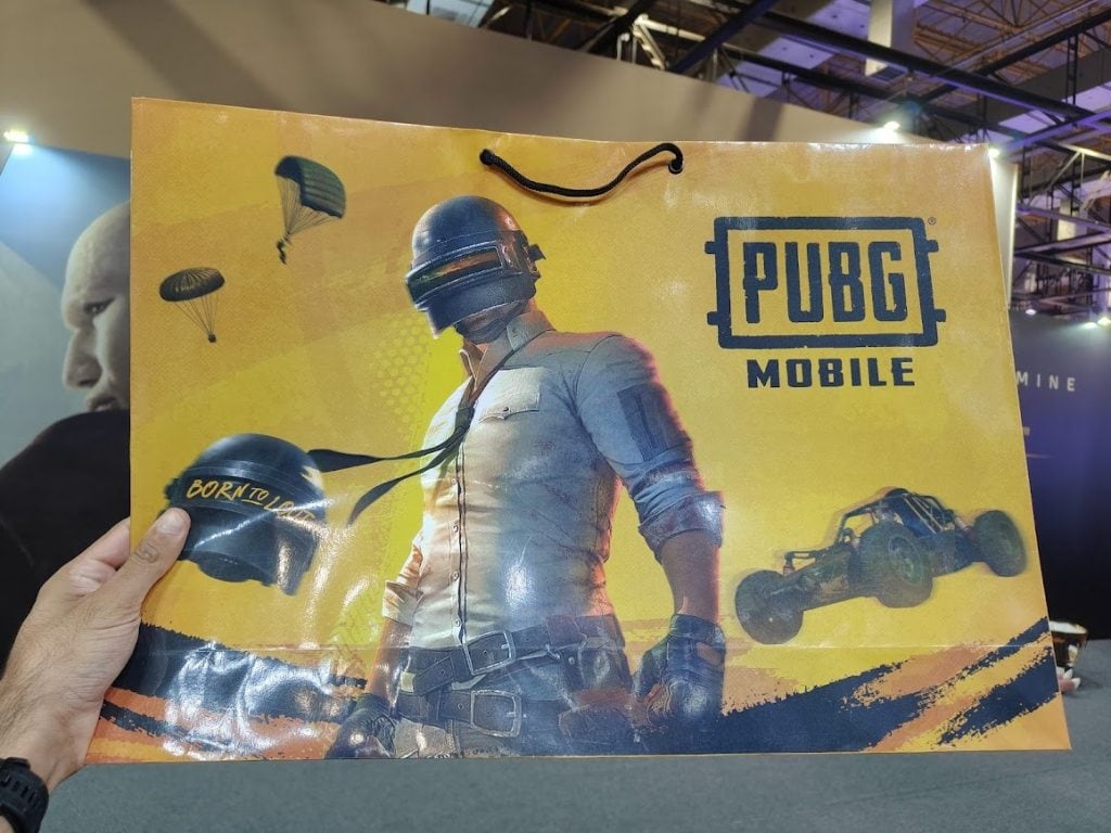 Capacete pubg mobile com personagem do jogo e carro de corrida em fundo amarelo, lançamento de game.