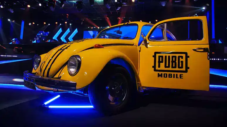 Volkswagen fusca pintado de amarelo com logo do pubg mobile em destaque, em ambiente de evento com iluminação vibrante.