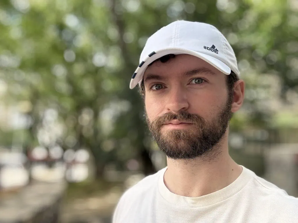 Anmeldelse: iPhone 16, hjemmehørende i en tidsalder av kunstig intelligens En skjeggete mann med hvit lue utendørs, fokusert på teknologi og livsstil.