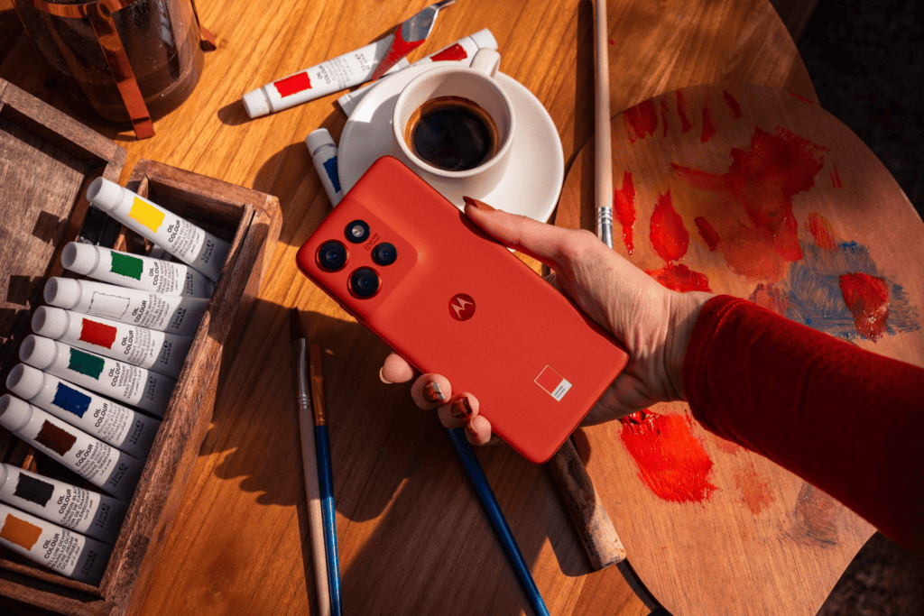 Câmera de smartphone motorola com fundo de pintura e café, tecnologia e criatividade em destaque.