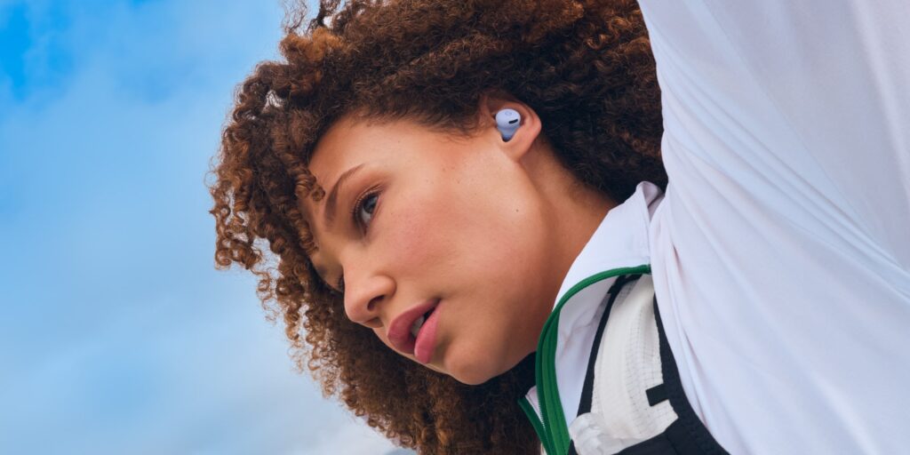 תוצרת גוגל: אוזניות Pixel Watch 4 ו-Pixel Buds 2a הוכרזו. אישה שחורה משתמשת ב-Pixel Buds 2a