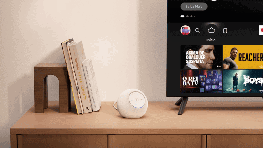Alt: alto-falante inteligente em setup de sala com televisão e livros modernos.