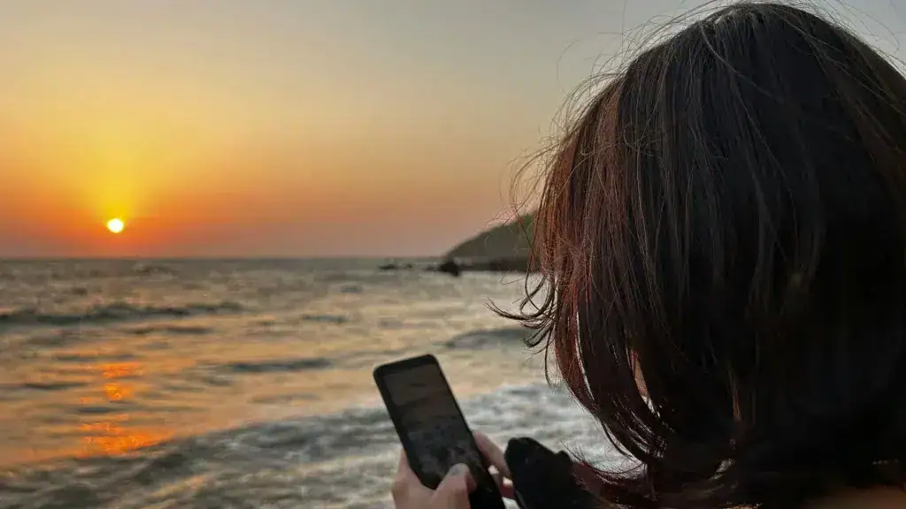 Hvordan beskytte elektronikk mot varme? Se tips og svar. Kvinne som bruker mobiltelefon på stranden.