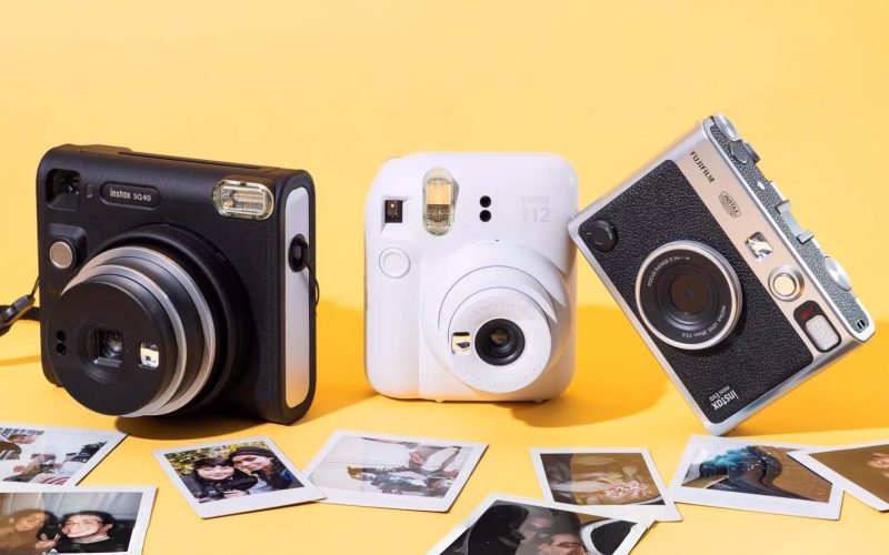 Câmeras instantâneas vintage e modernas em fundo amarelo com fotos impressas na mesa.