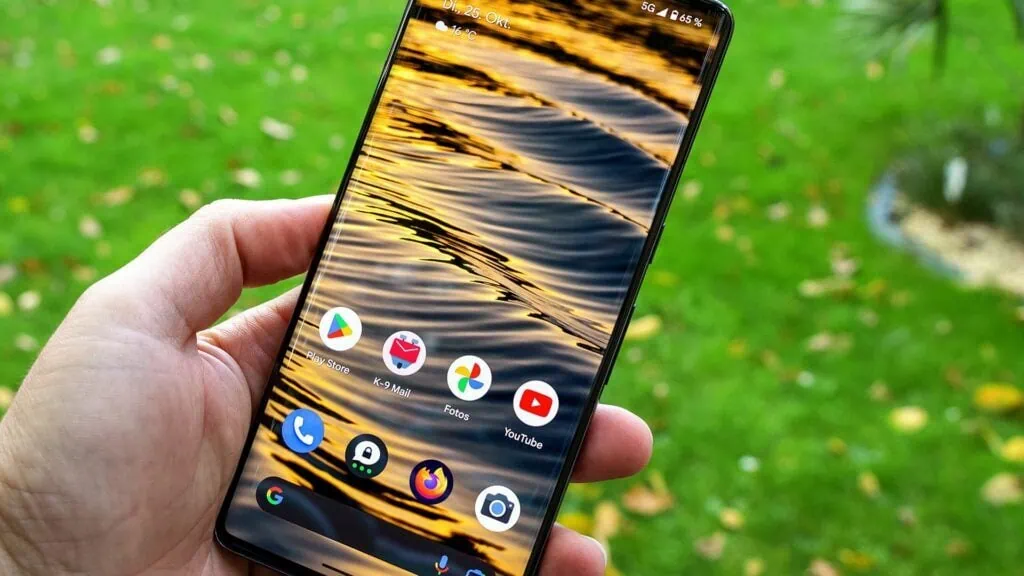 A história do android (versão 1 a 16) Smartphone exibindo ícones de aplicativos android, com fundo de água refletindo o pôr do sol.