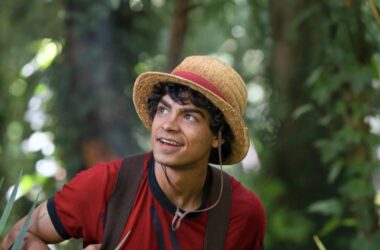 Imagem de jovem sorridente com chapéu em floresta.