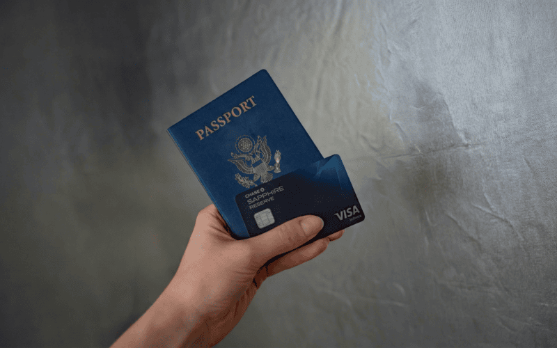 Mão segurando passaporte com cartão visa contra parede cinza.