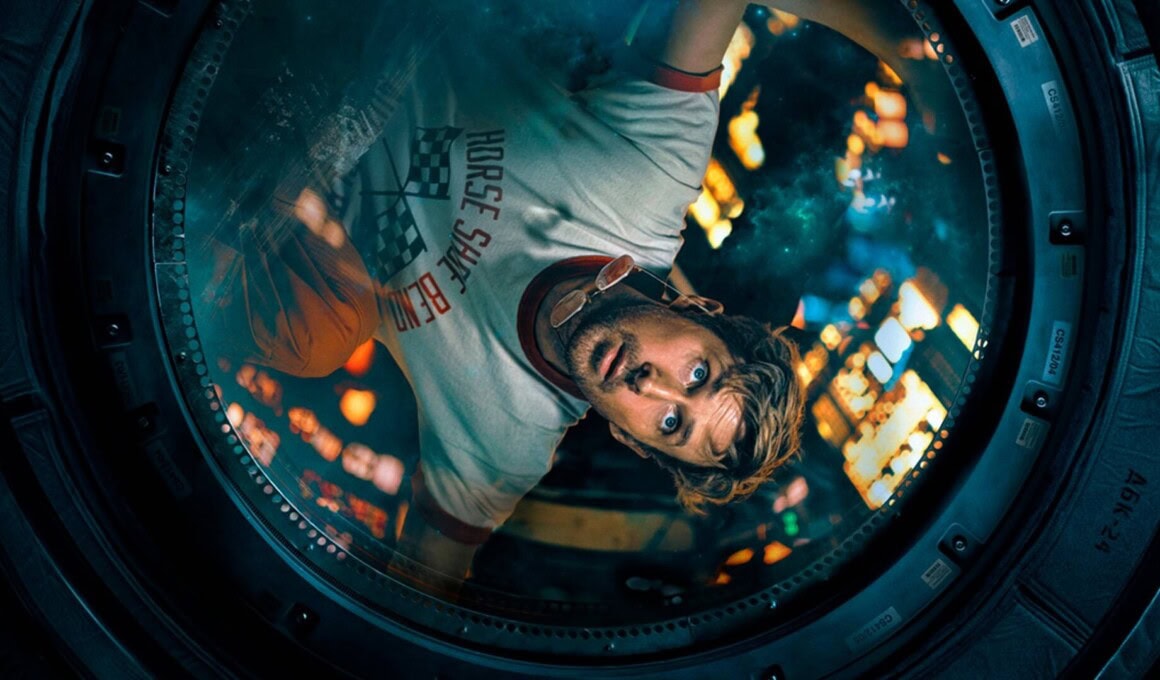 Imagem de um jovem olhando através de uma máquina de lavar roupa, com luzes de cidade ao fundo.