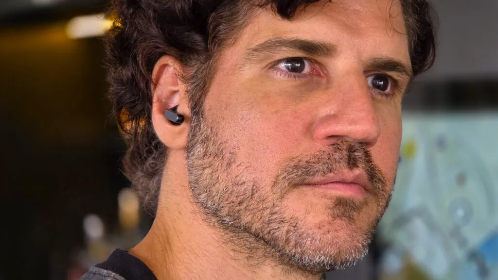 Review: galaxy buds4 pro, melhor que airpods Fone de ouvido galaxy buds4 pro preto no ouvido de um homem com barba.