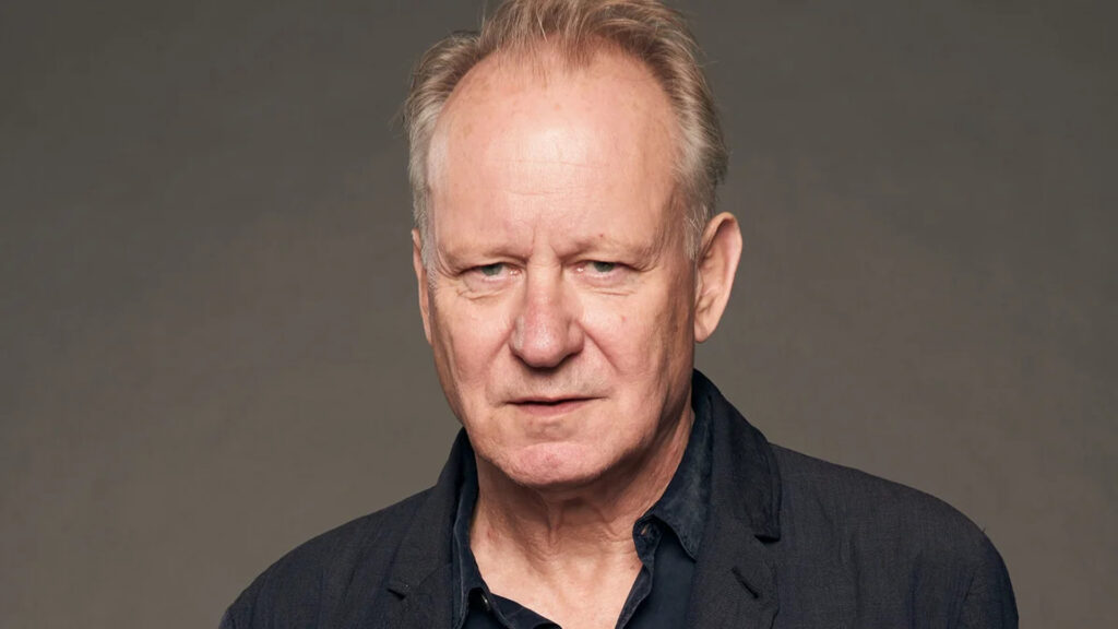 Foto de perfil do ator stellan skarsgard usando uma blusa de botão azul escura
