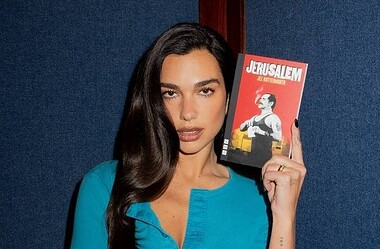 Dua lipa segura o livro jerusalem diante de fundo azul em retrato vertical.