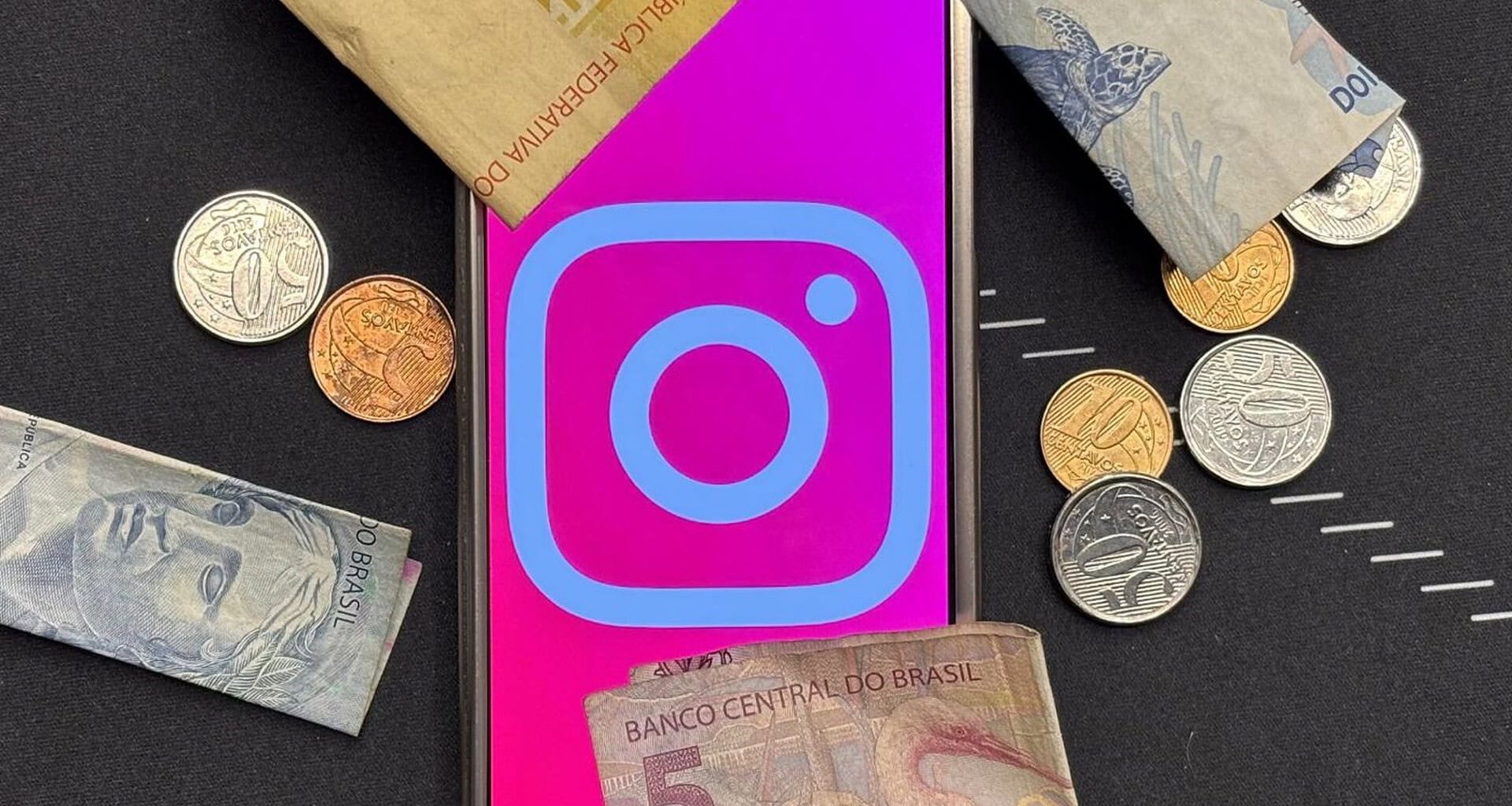 Celular com o logo do instagram cercado por cédulas e moedas de real brasileiro, representando a assinatura paga instagram plus.