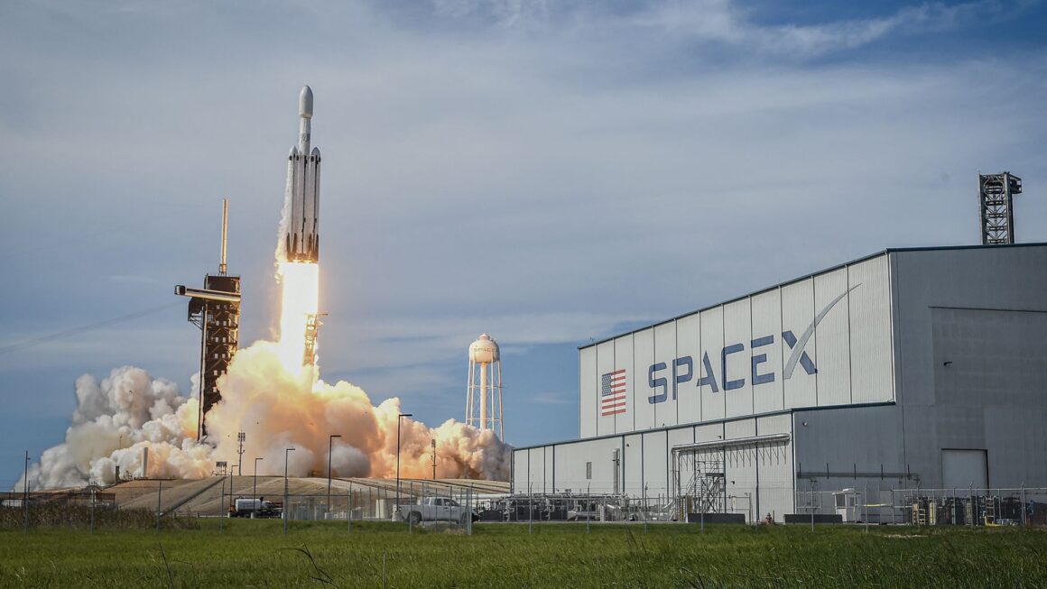 Foguete falcon heavy da spacex decolando ao lado de prédio com logotipo da empresa