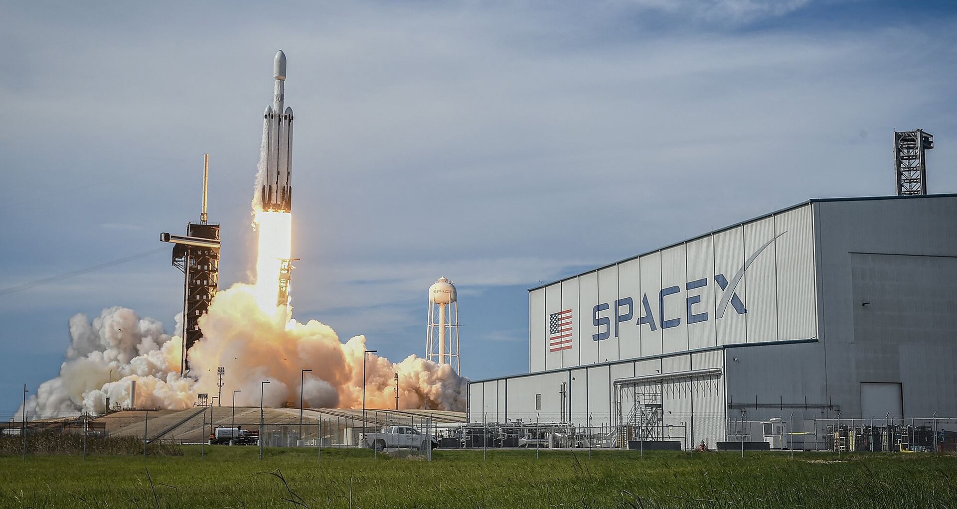 Foguete falcon heavy da spacex decolando ao lado de prédio com logotipo da empresa