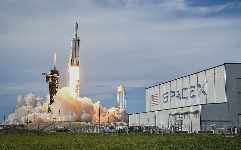 Foguete falcon heavy da spacex decolando ao lado de prédio com logotipo da empresa