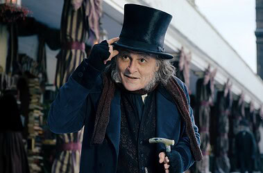 Johnny depp caracterizado como ebenezer scrooge toca a cartola em uma rua vitoriana