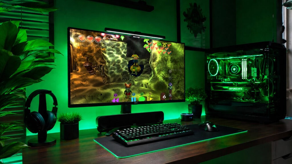 Monitor widescreen exibe gameplay do jogo blinx rodando via retrocompatibilidade de xbox no pc em uma mesa gamer com iluminação verde.