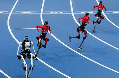 Cinco robôs humanoides correm em uma pista azul durante competição em pequim